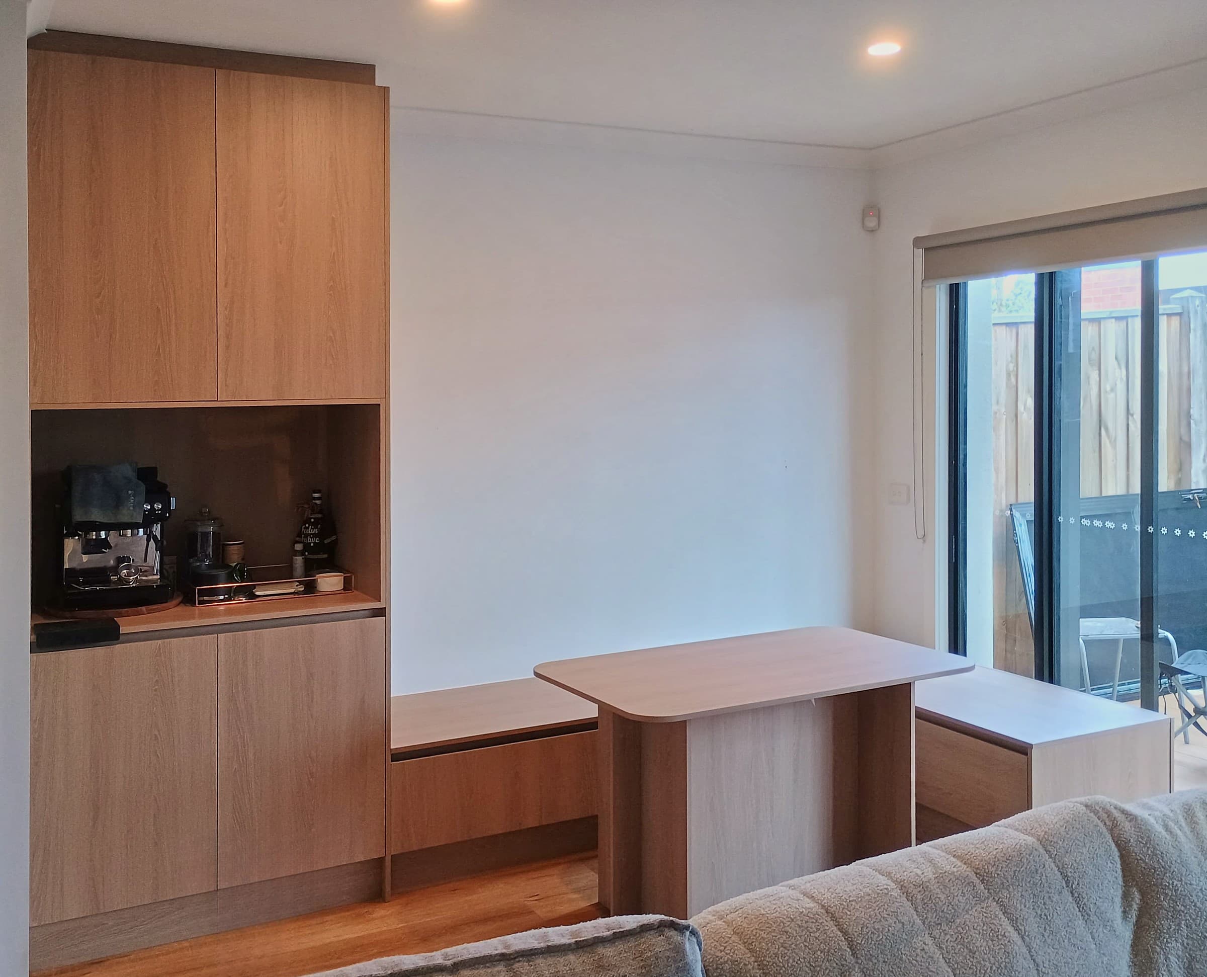 Built-in coffee station in light oak-look laminate, flowing into a custom dining bench and table.