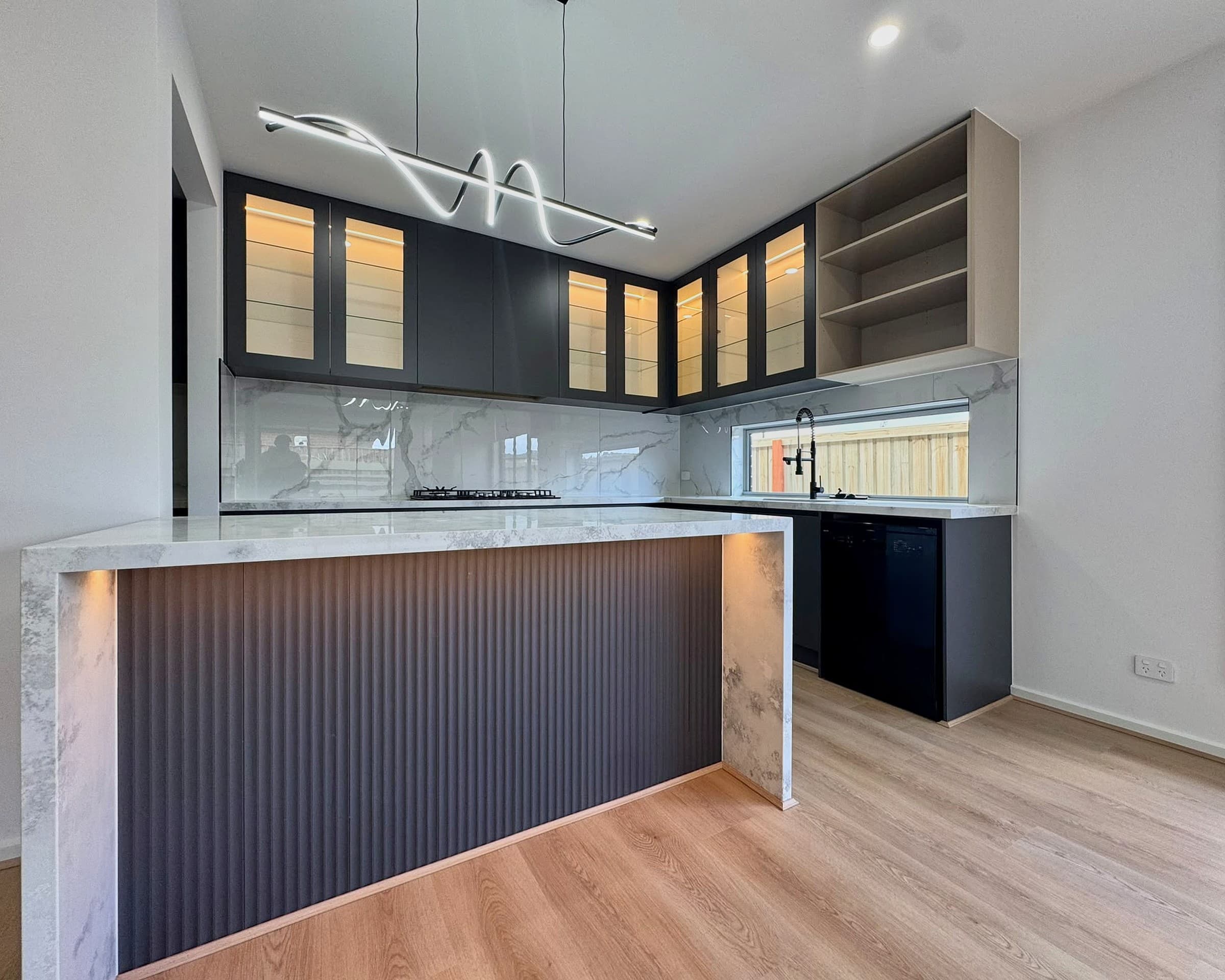 Charcoal kitchen with glass-front display uppers, fluted island panel and marble-look waterfall benchtop.